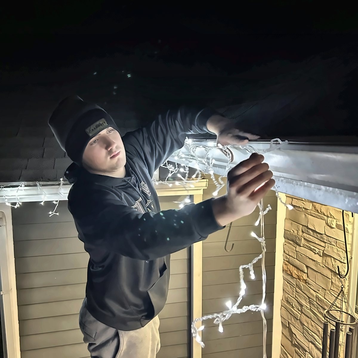 Dylan hanging icicle lights along a gutter at night